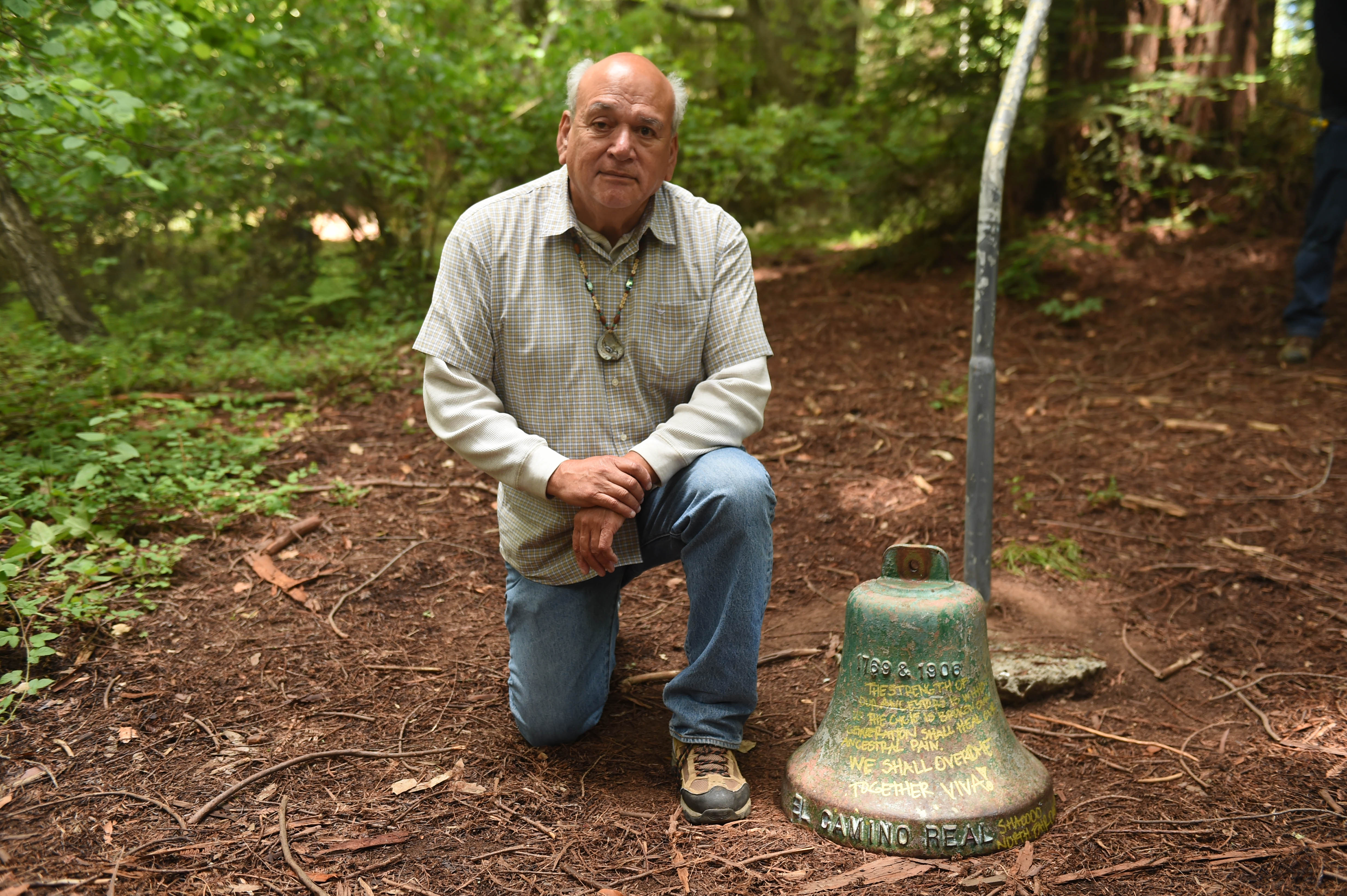 Chairman Val Lopez kneeling by a bell