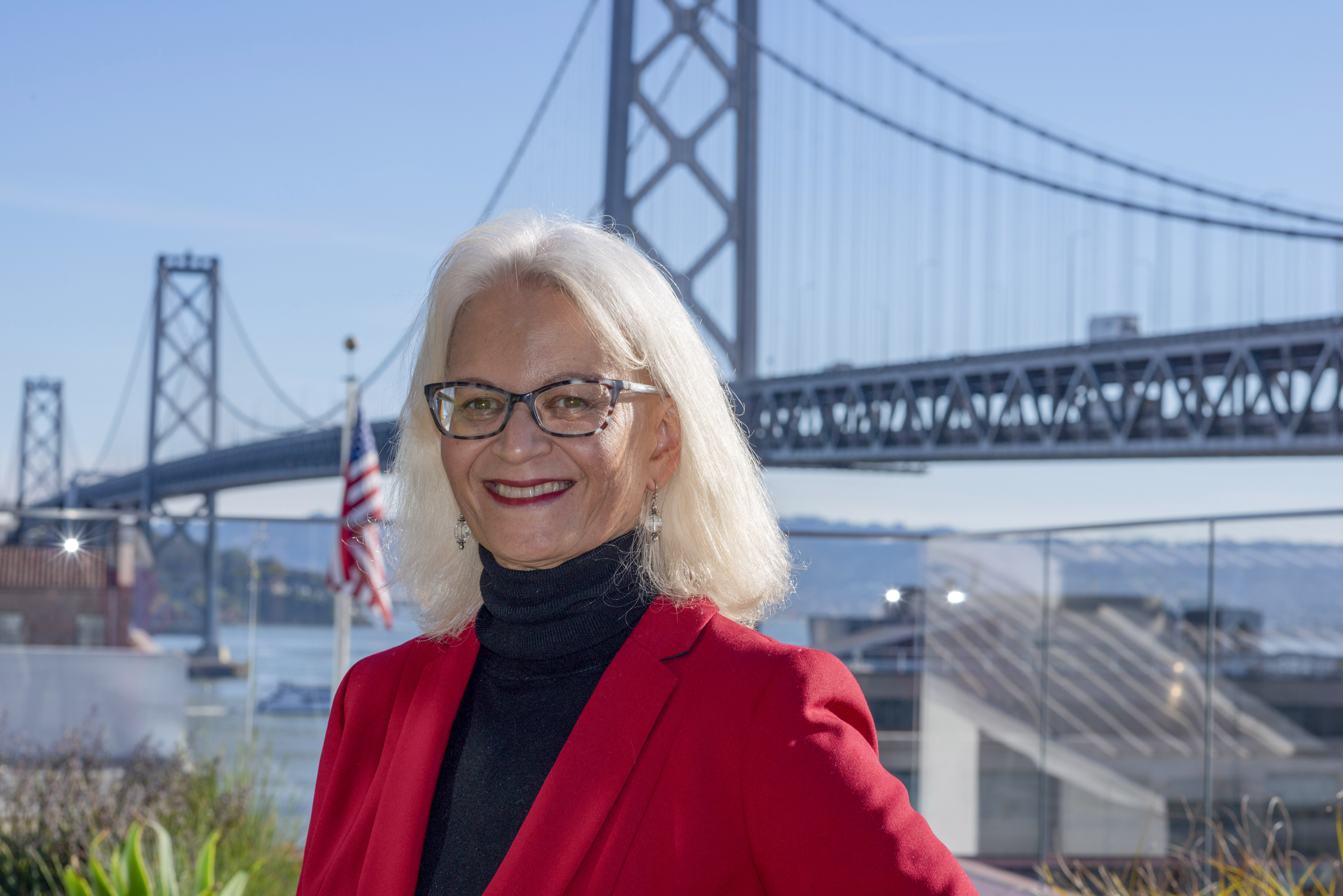 Therese McMillan wearing red blazer in front of Bay Bridge